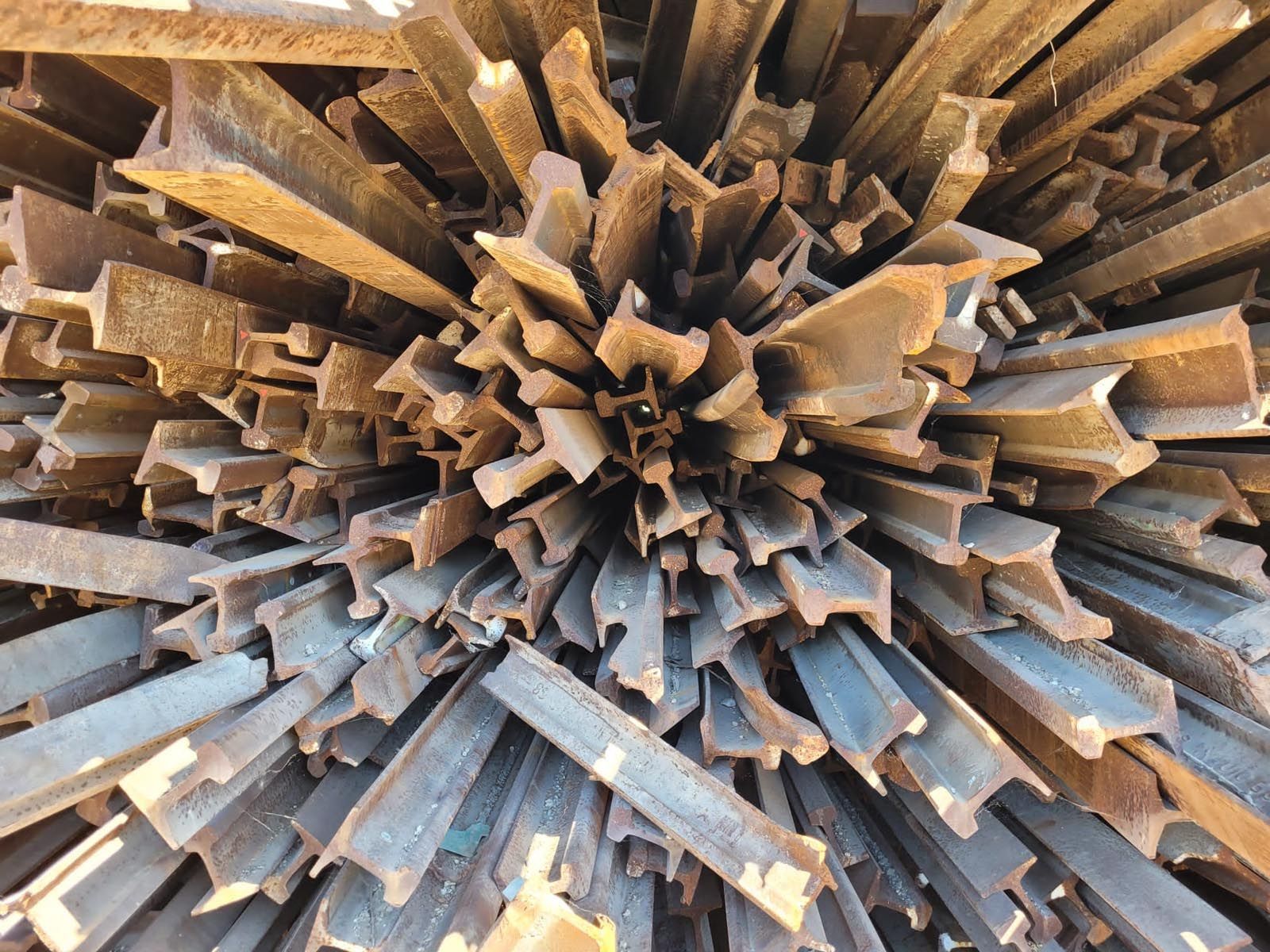 Un tas de morceaux de rails métalliques rouillés, disposés en cercle, vus du dessus au soleil.