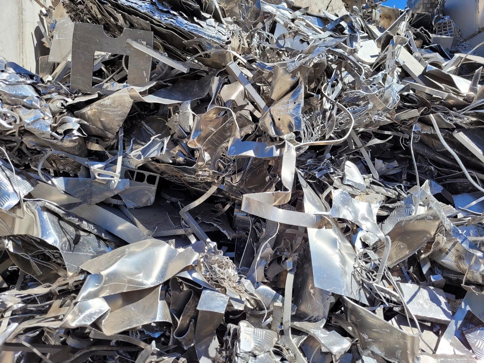 Tas de ferraille brillante et broyée, probablement destinée au recyclage, à l'extérieur.