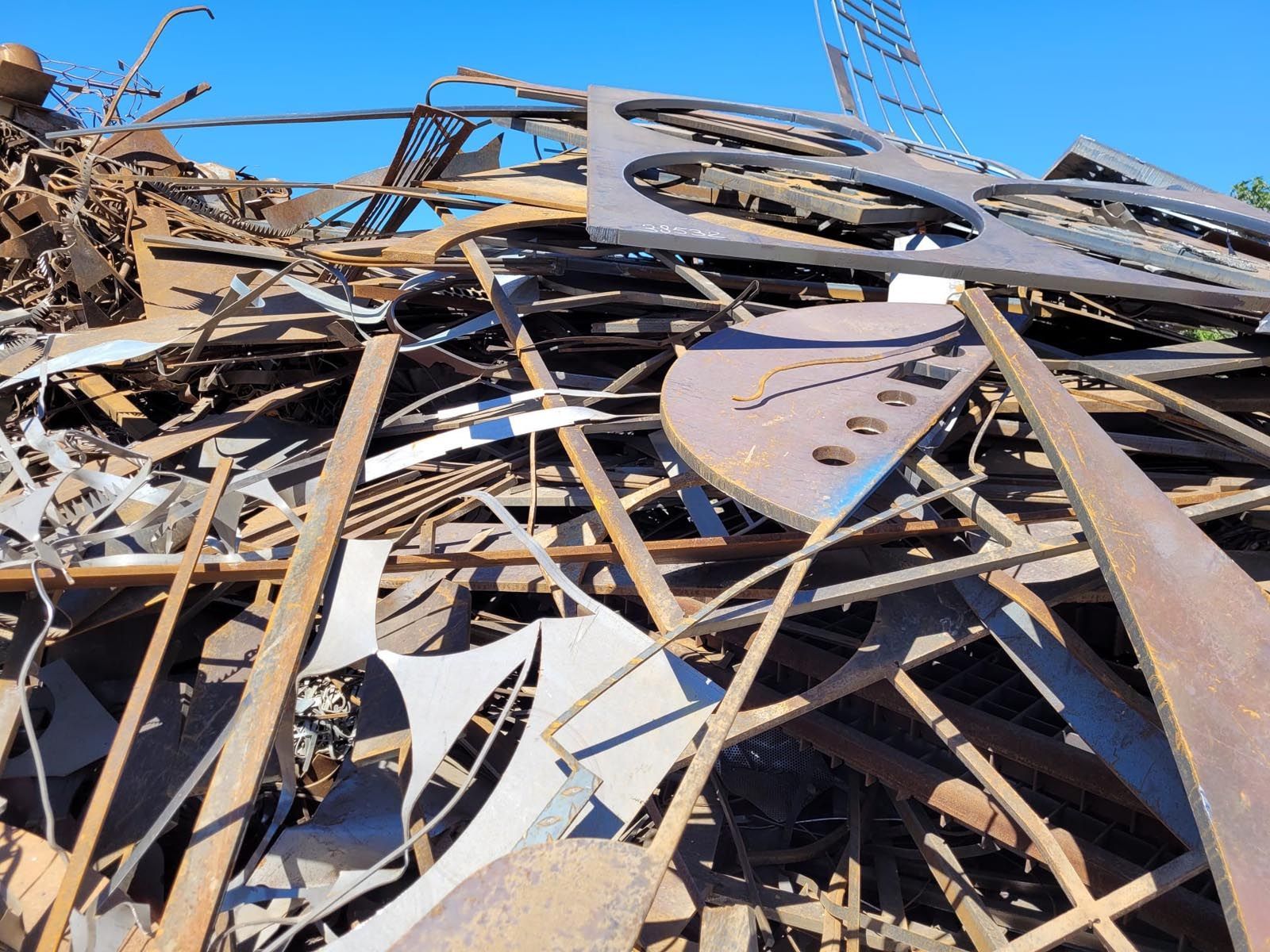 Un tas de ferraille se détachant sur un ciel bleu clair, comprenant des formes d'acier découpées, des poutres et des barres.