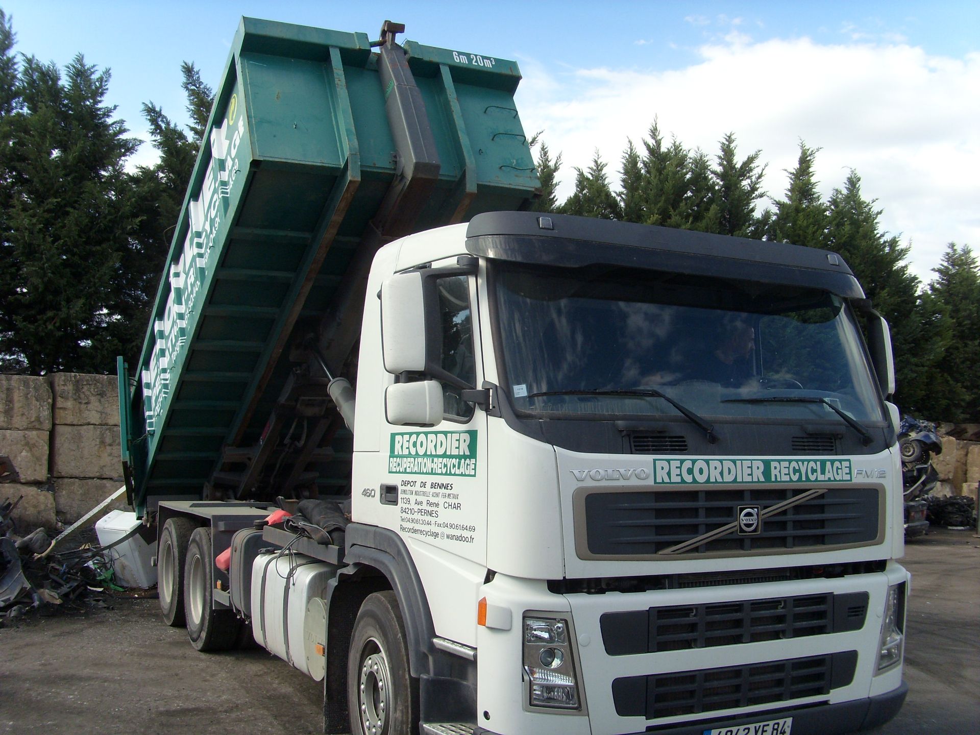 Une benne à déchets verts est soulevée par un camion blanc des ETS ANDRE RECORDIER dans le centre de recyclage.