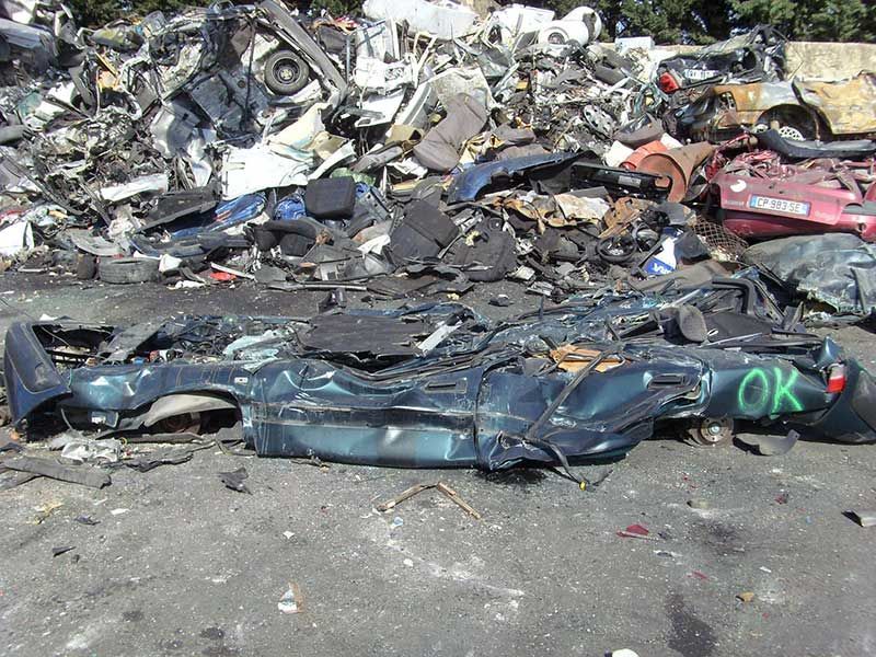 Un tas de véhicules broyés dans une casse, dont une voiture bleue portant l'inscription OK.