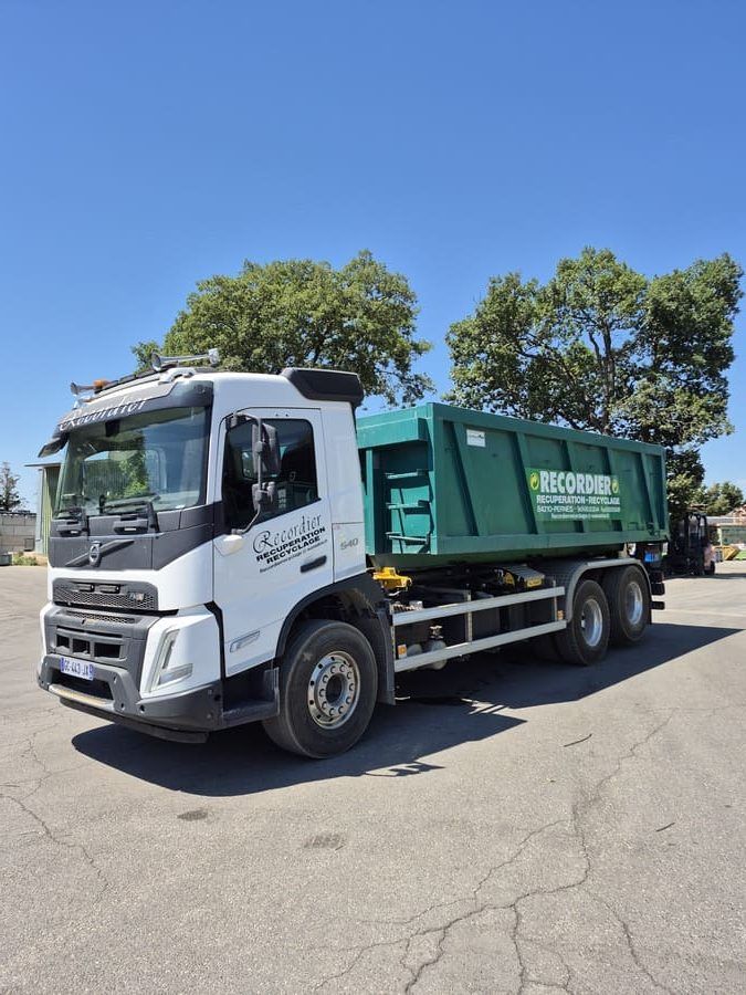 Camion blanc des ETS ANDRE RECORDIER avec une benne à ordures verte par une journée ensoleillée.