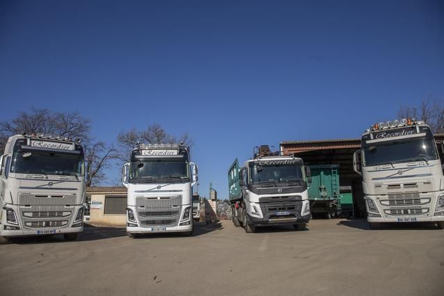 Quatre camions blancs garés devant un bâtiment sous un ciel bleu azur.