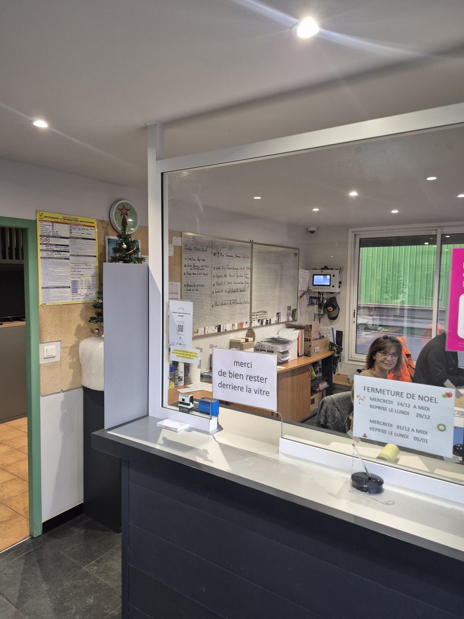 Espace d'accueil : une personne est assise à un bureau, regardant par la fenêtre. Comptoir, documents et inscriptions murales.