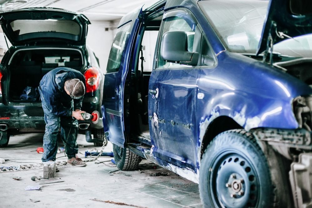 Un hombre está trabajando en una camioneta azul en un garaje.