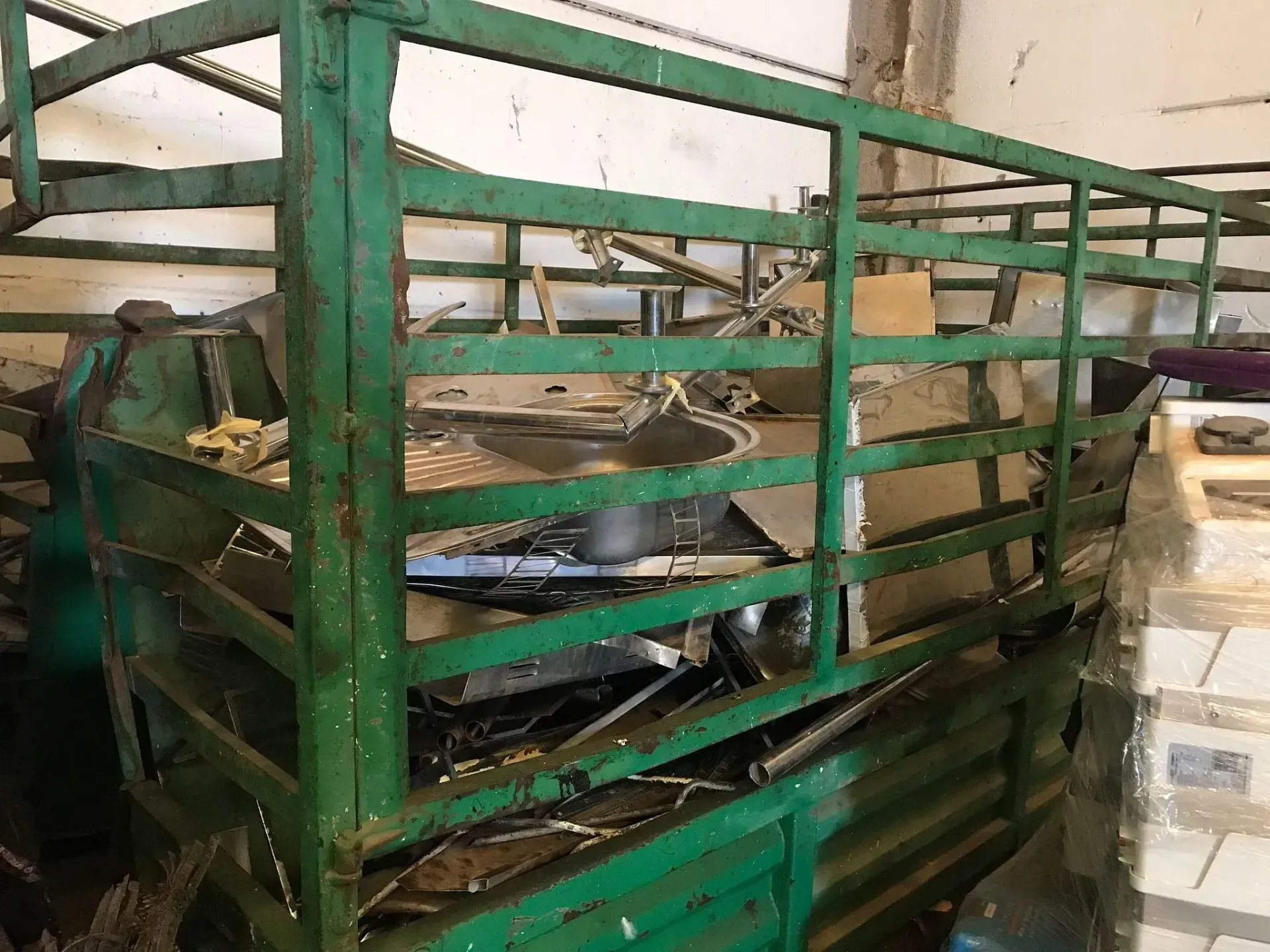 Una jaula verde llena de basura en un almacén.