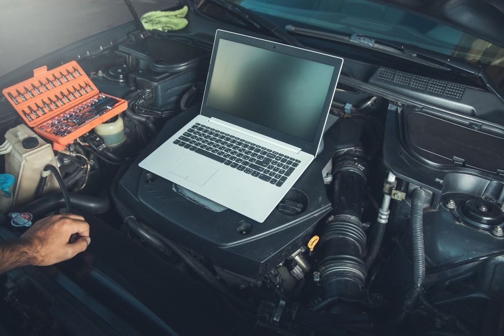 Una computadora portátil está colocada encima del motor de un automóvil.