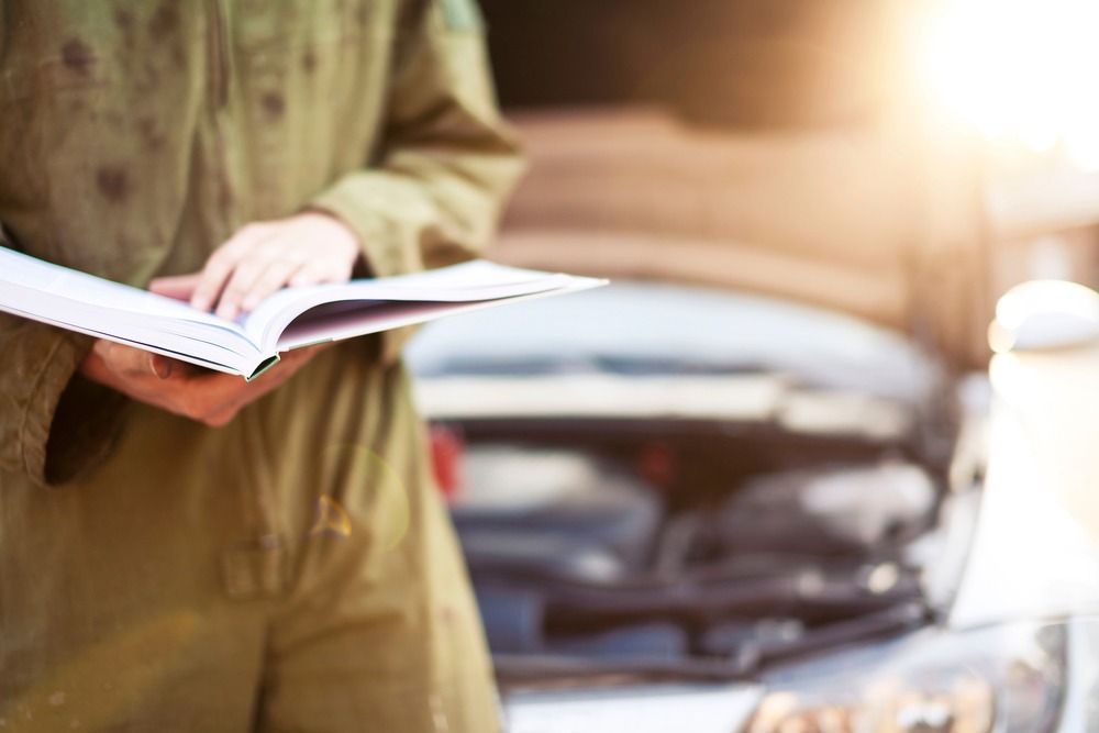 Un mecánico está leyendo un manual mientras está de pie junto a un automóvil.