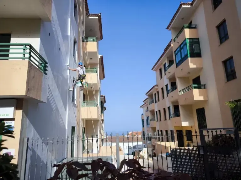 Patio soleado del apartamento con balcones y puerta negra, montañas en la distancia.