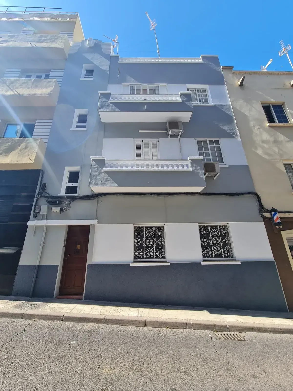 Edificio de apartamentos azul de tres plantas con balcones y aire acondicionado en una calle soleada.