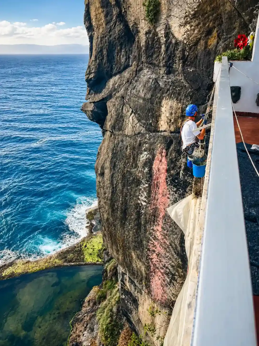 Escalador ascendiendo un escarpado acantilado costero junto al océano azul y una pared de roca blanca.