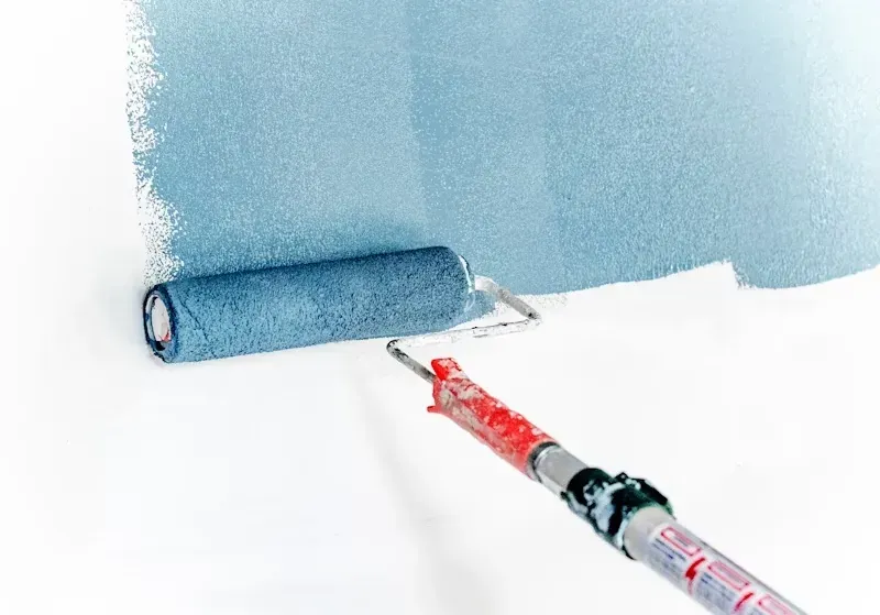 Un rodillo aplica pintura azul claro a una pared con una brocha en primer plano.