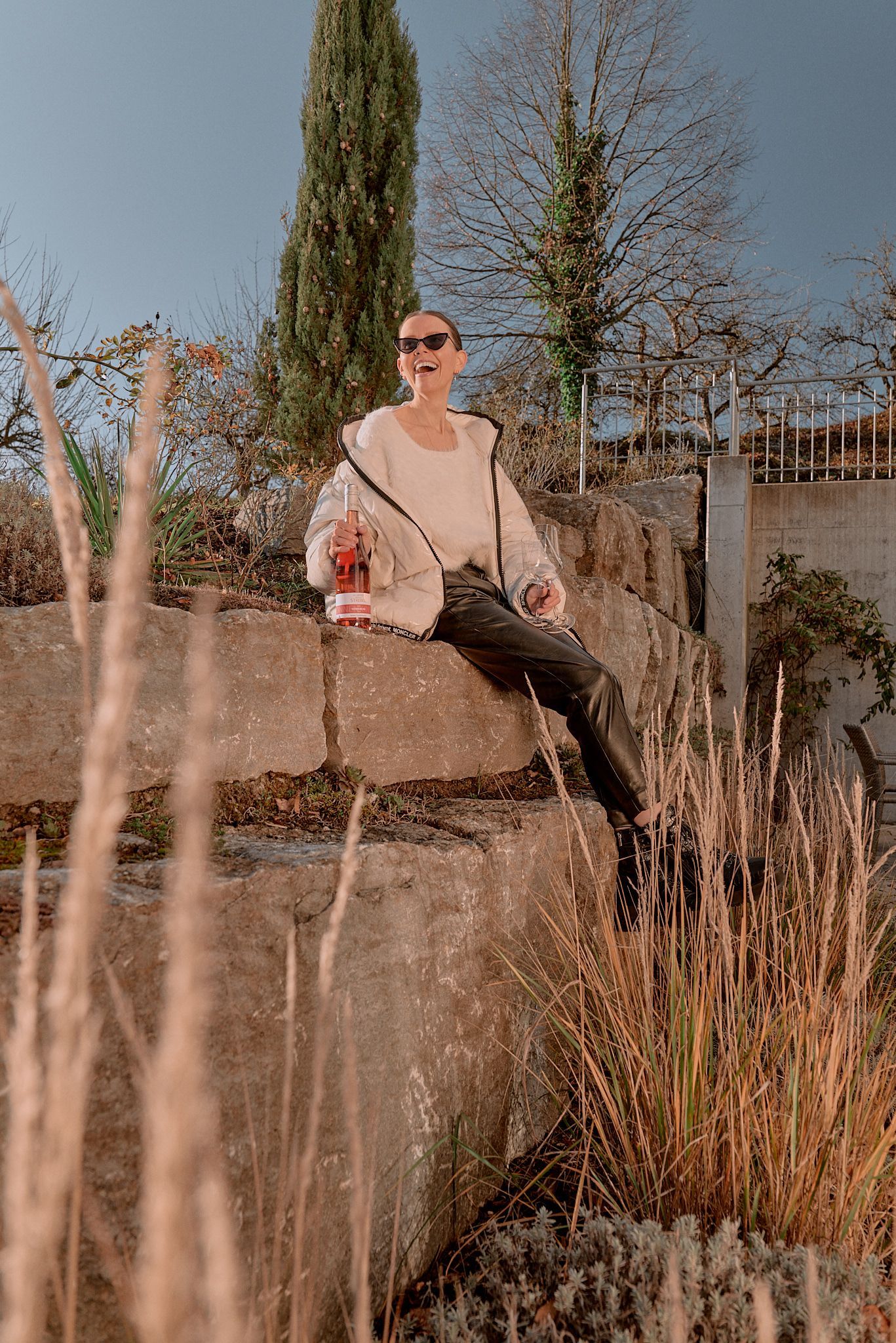 Eine Frau sitzt auf einer Mauer auf einem Feld und hält etwas zu trinken.