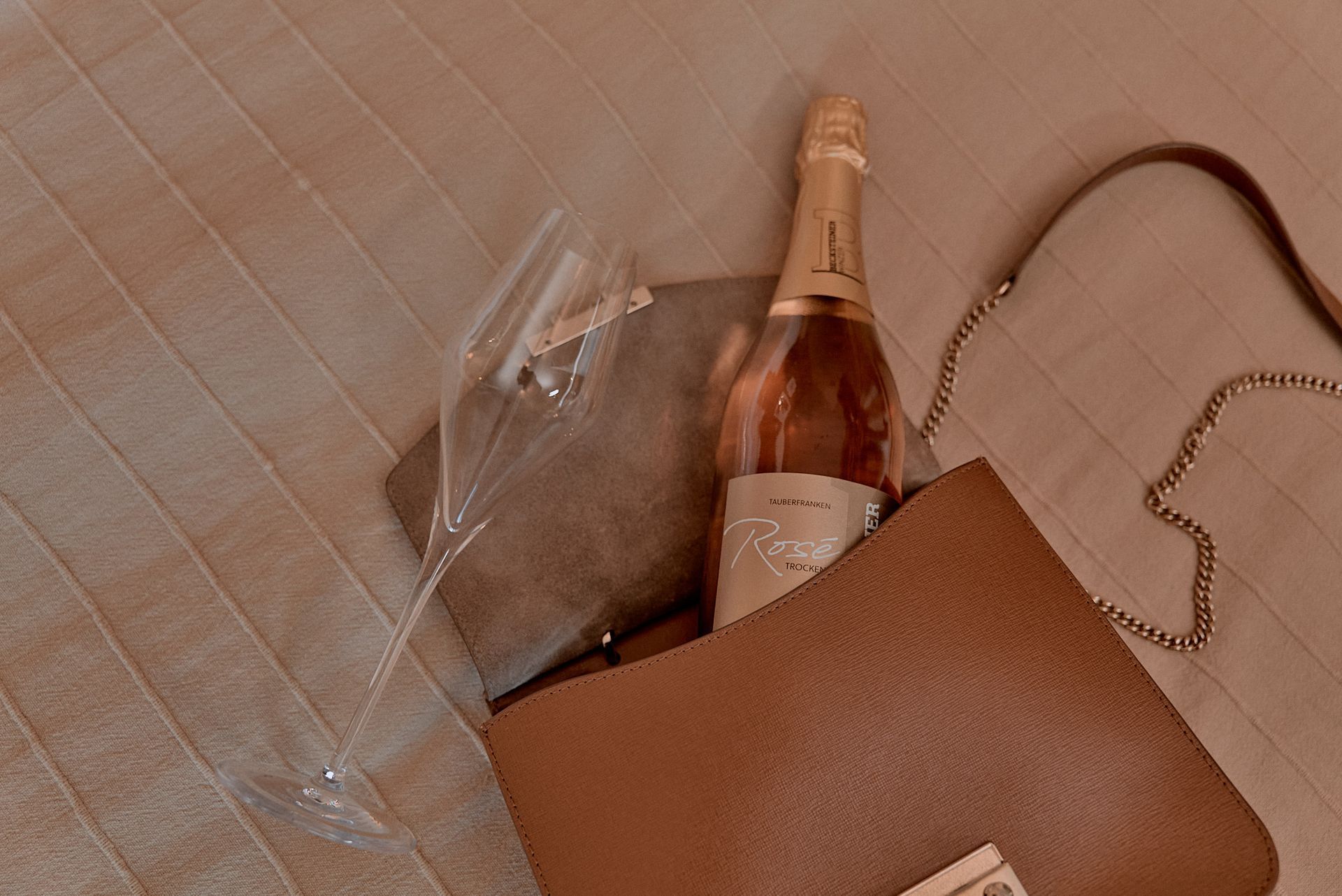 In einer braunen Handtasche befinden sich eine Flasche Wein und ein Glas Wein.
