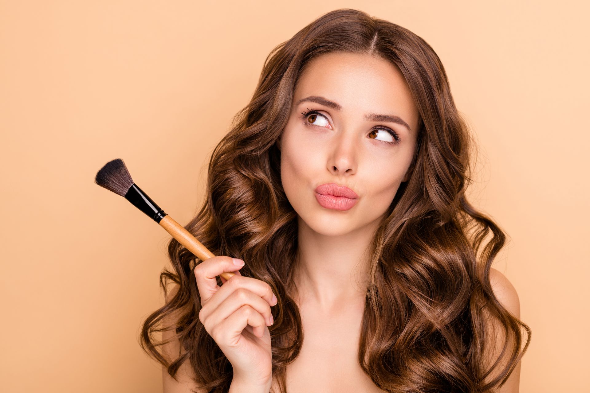 Eine Frau hält einen Make-up-Pinsel in der Hand und macht ein lustiges Gesicht.