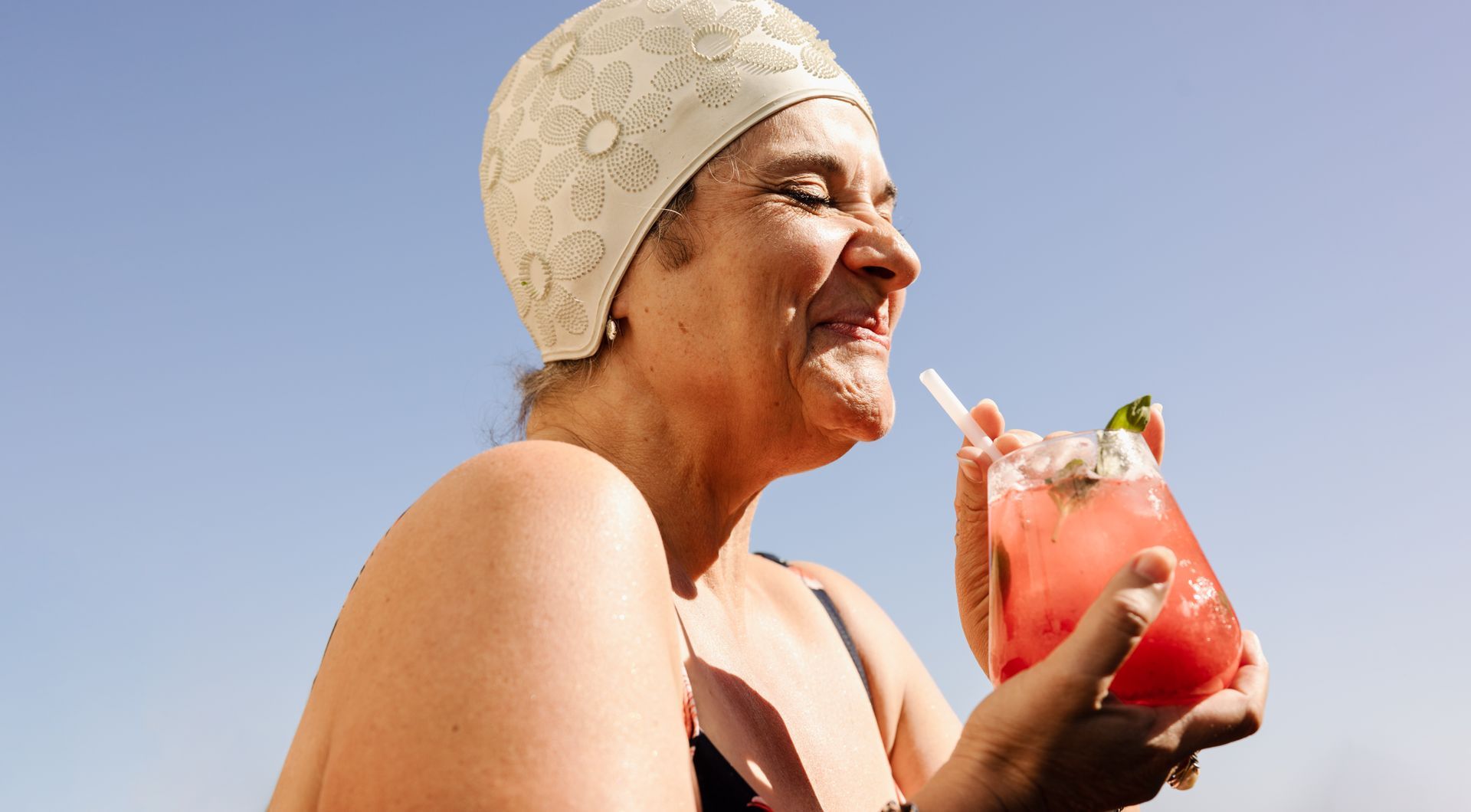 Eine Frau mit Badekappe trinkt mit einem Strohhalm aus einem Glas.