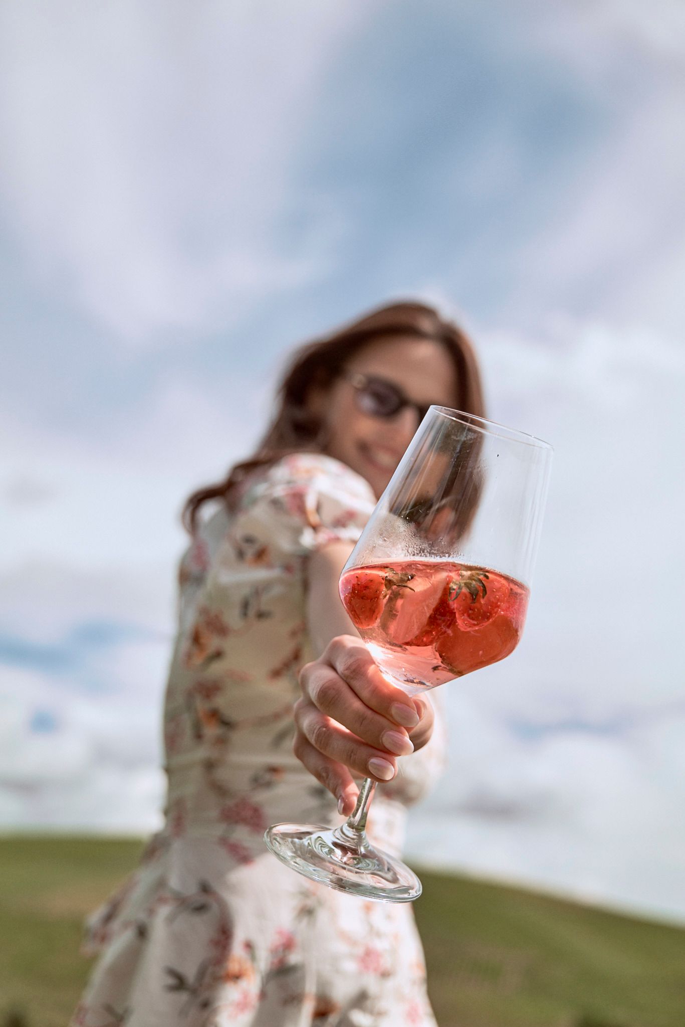 Eine Frau hält ein Glas Wein mit Erdbeeren darin.