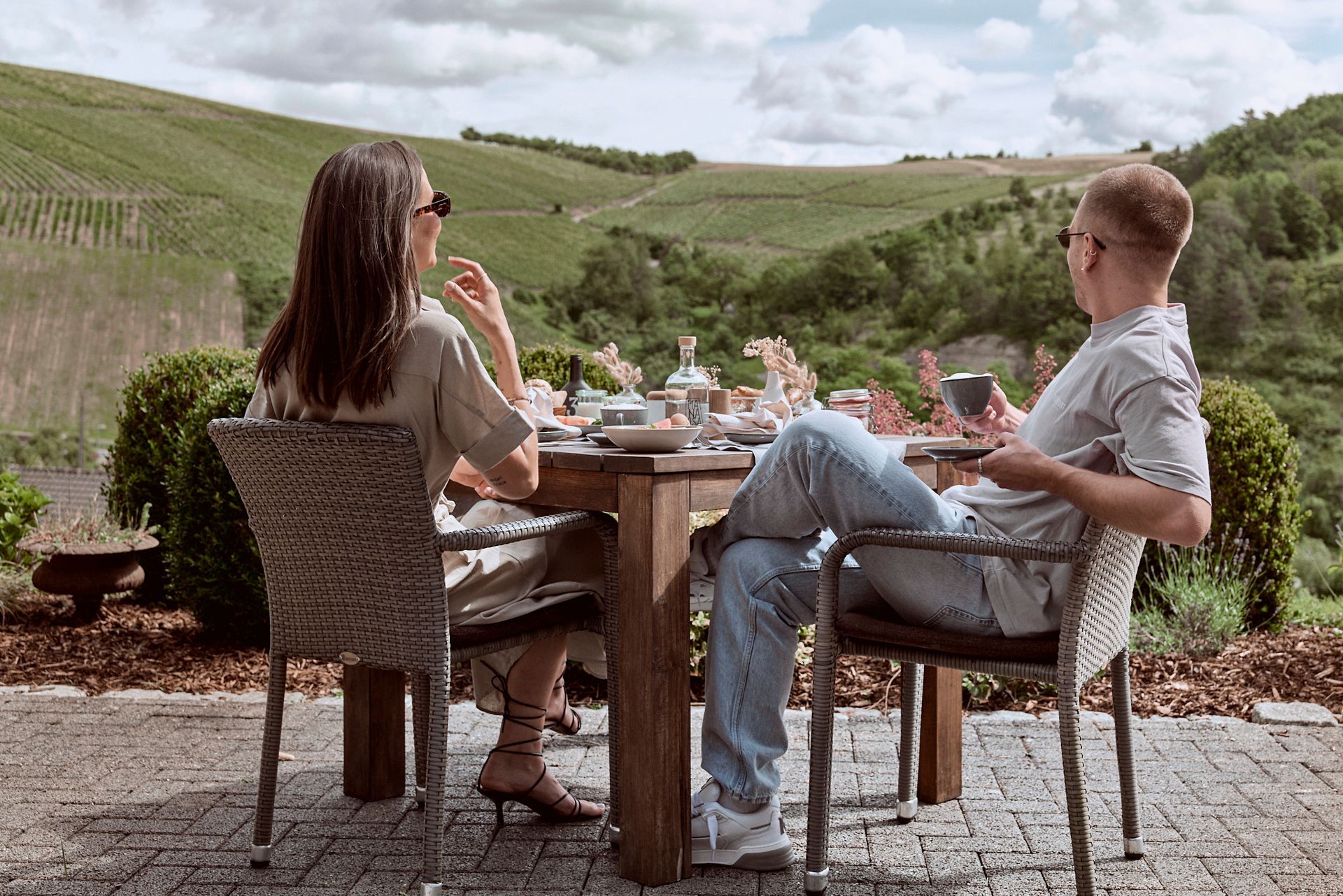 Ein Mann und eine Frau sitzen an einem Tisch mit Blick auf einen Weinberg.