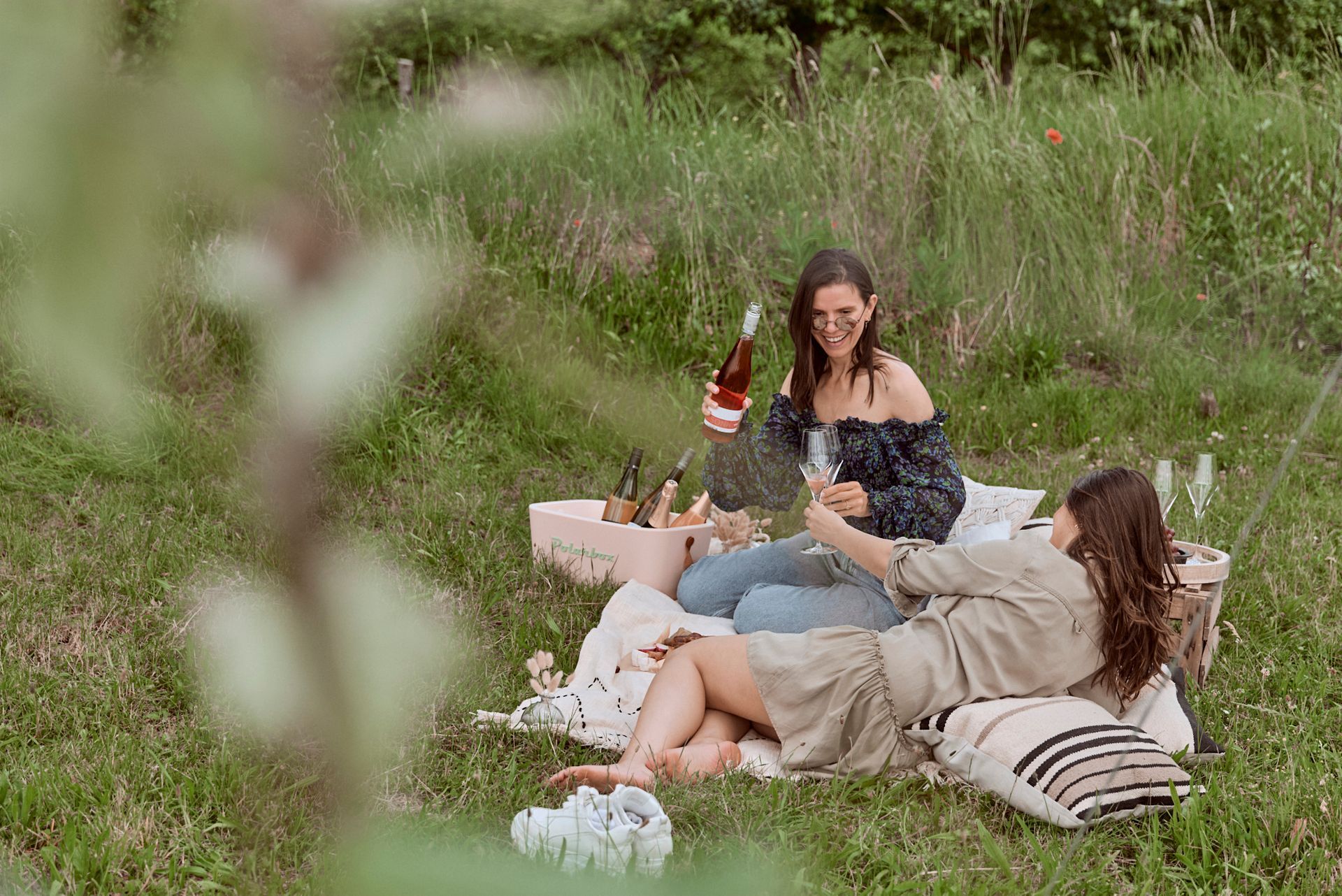 Zwei Frauen machen ein Picknick im Gras und trinken Wein.