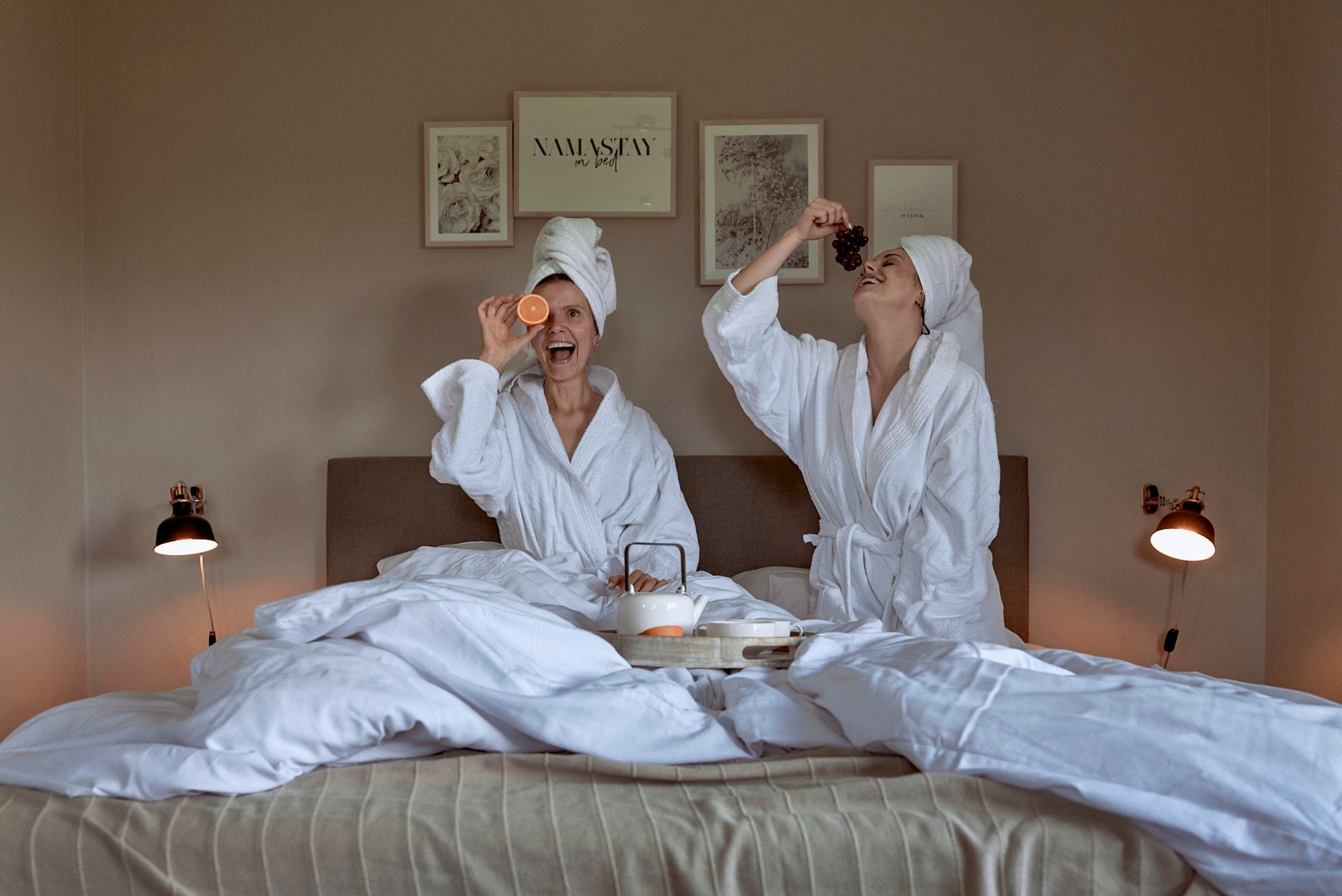 Zwei Frauen in Bademänteln sitzen auf einem Bett und trinken Tee.