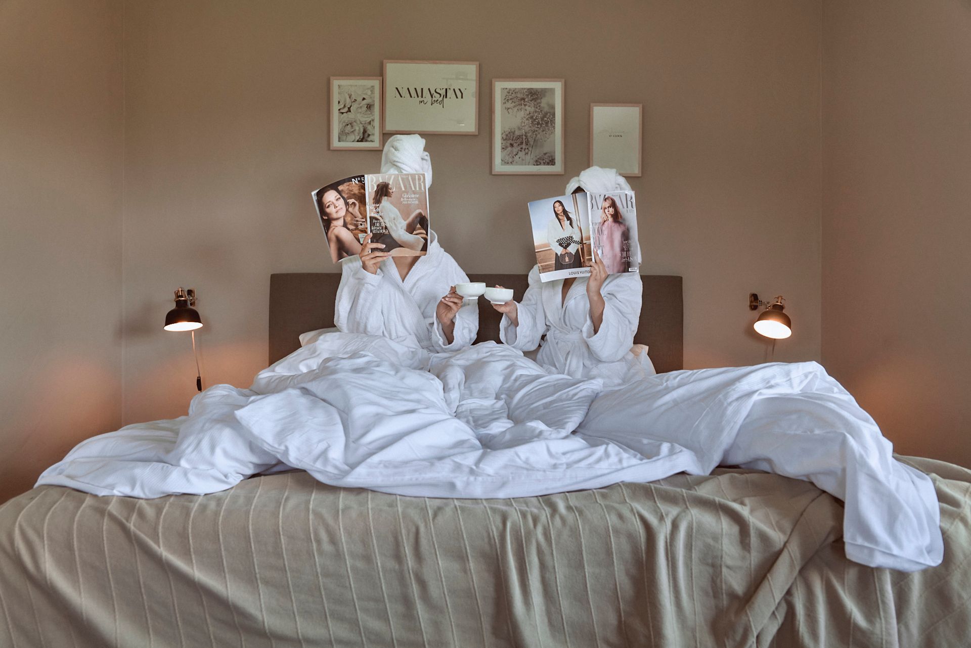 Zwei Frauen sitzen auf einem Bett und ihre Gesichter sind auf einer Zeitschrift abgebildet.