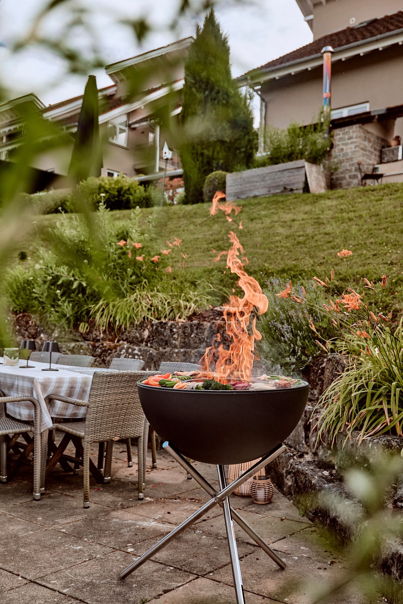 Auf einer Terrasse steht neben einem Tisch und Stühlen eine Feuerstelle.