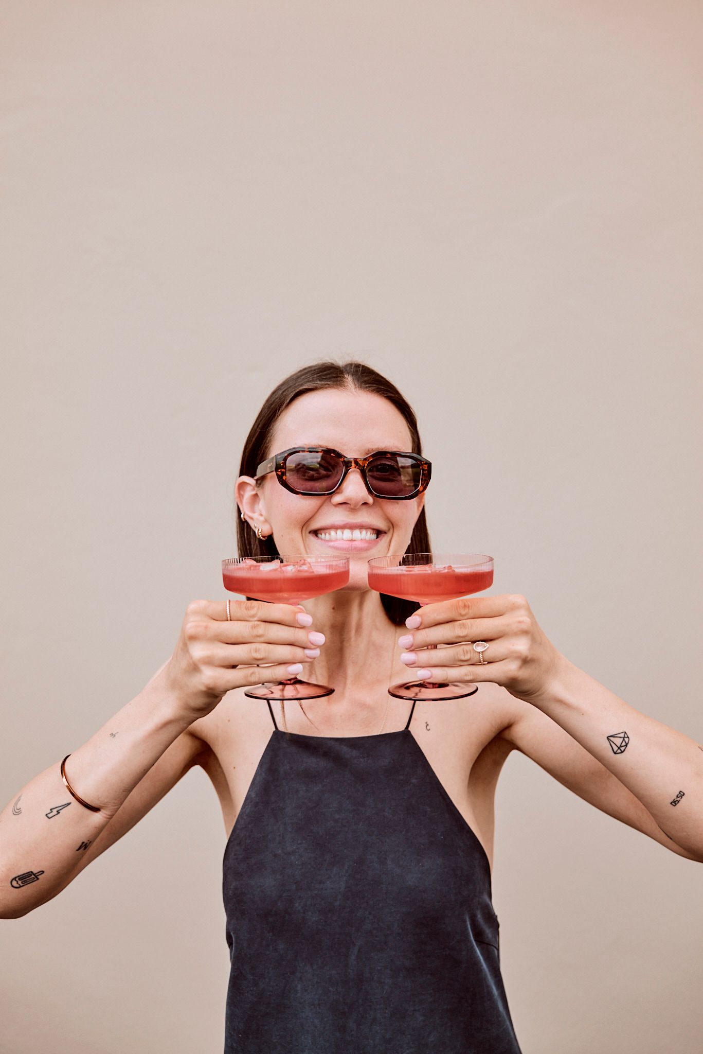 Eine Frau mit Sonnenbrille hält zwei Gläser Wein in ihren Händen.
