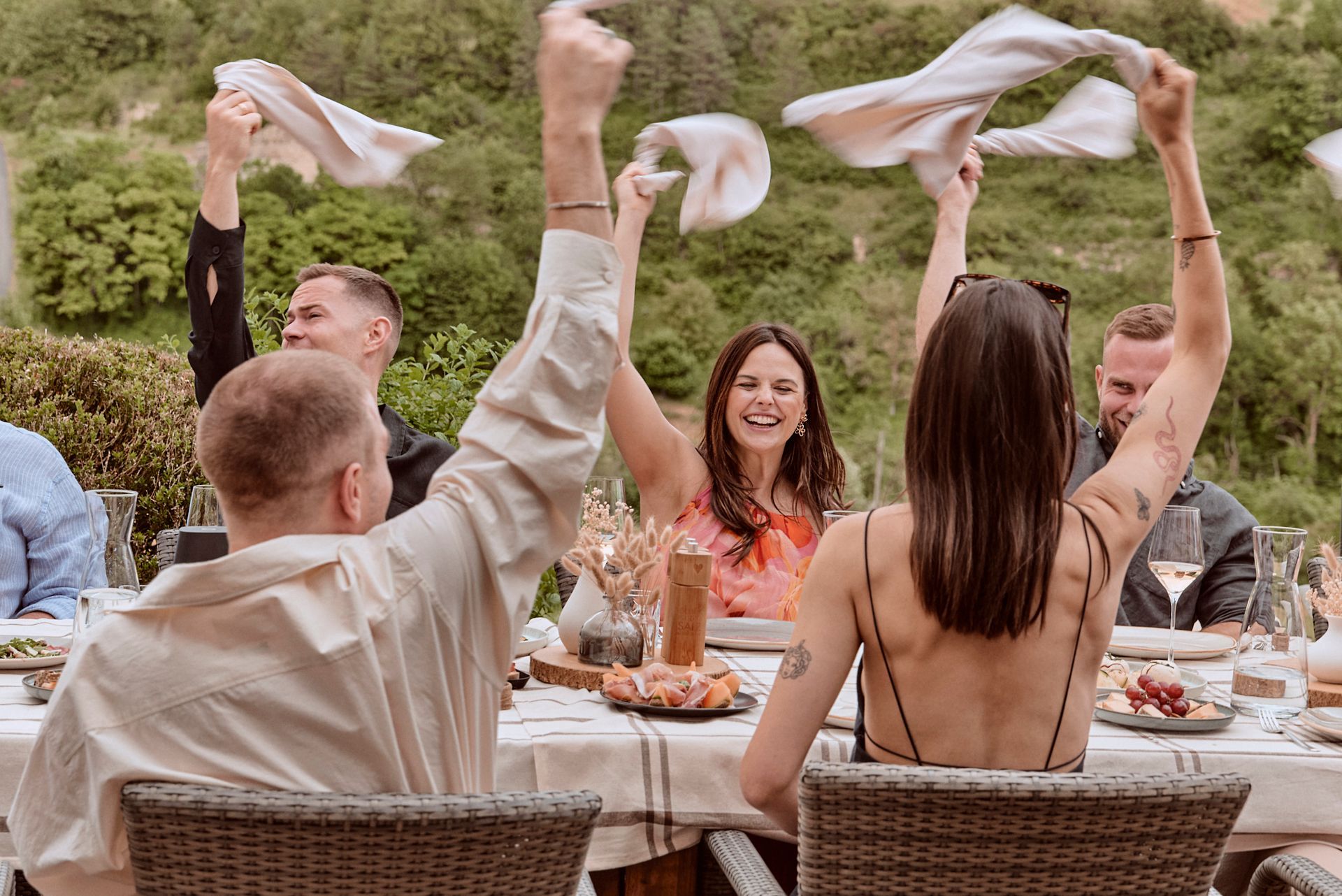 Eine Gruppe von Leuten sitzt mit erhobenen Armen an einem Tisch.