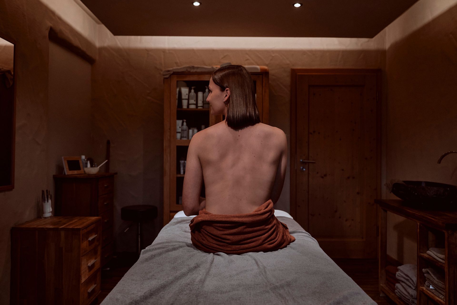 Eine Frau sitzt in einem dunklen Raum auf einem Massagetisch.