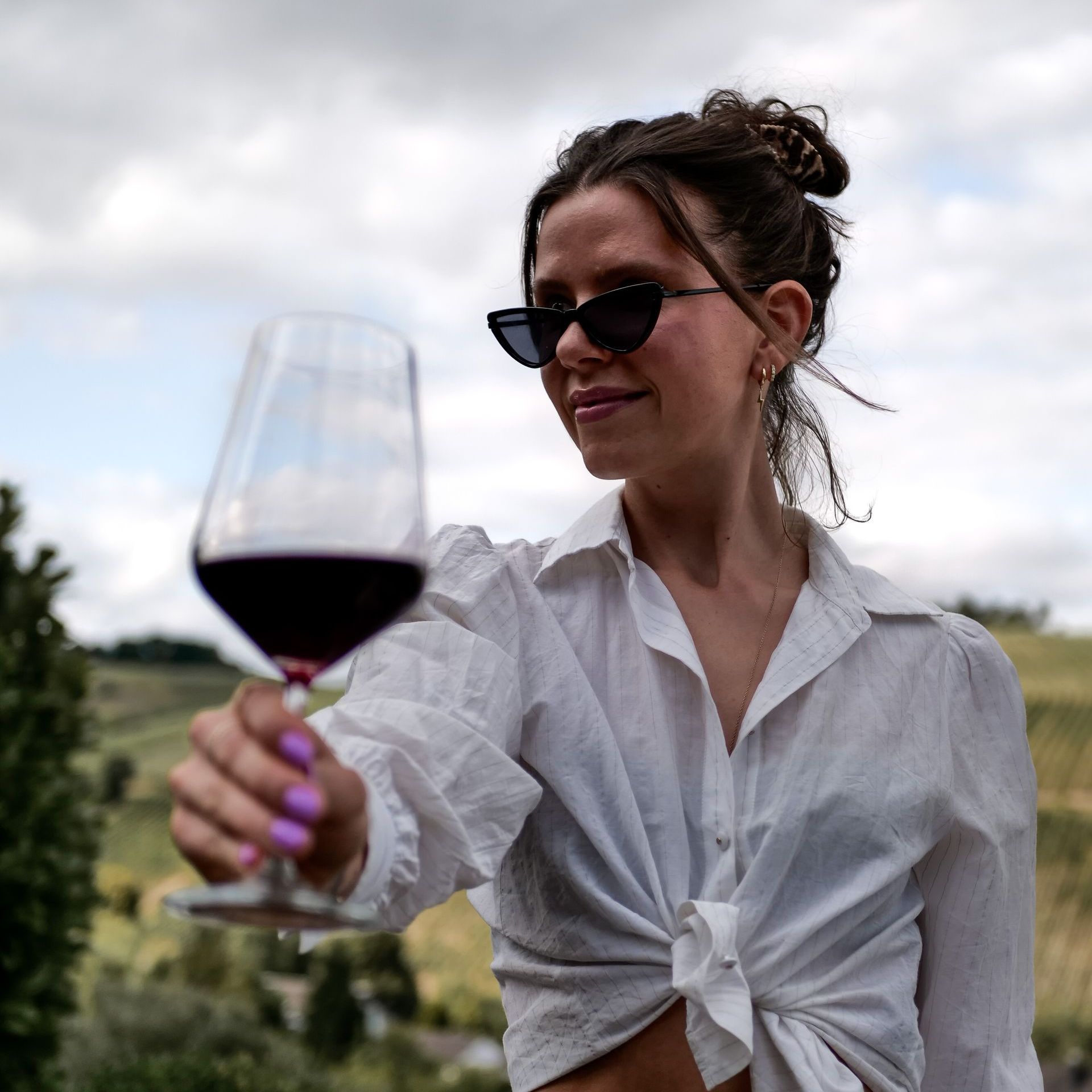 Eine Frau mit Sonnenbrille hält ein Glas Rotwein.