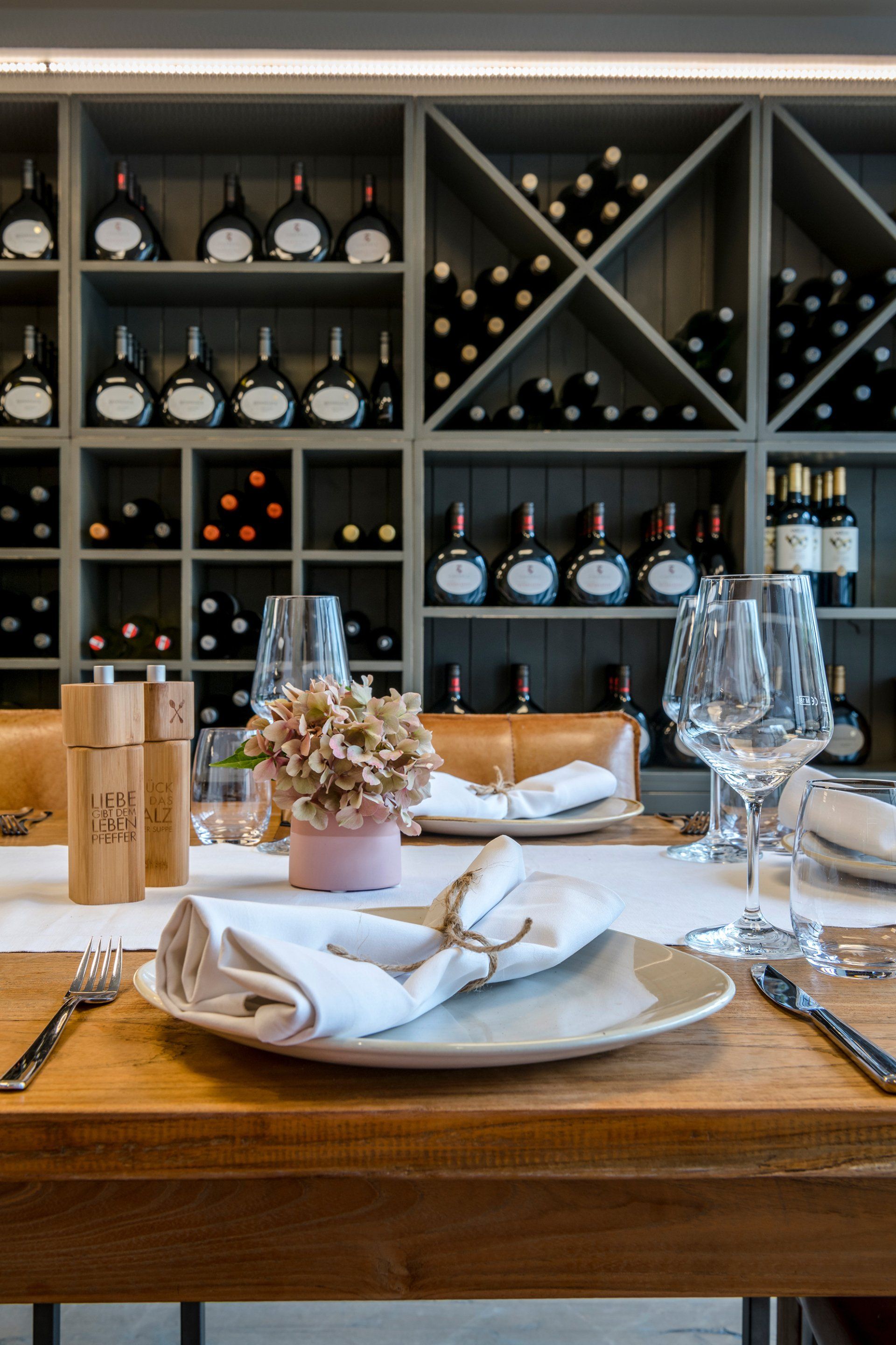Ein Holztisch mit Tellern, Gläsern und einer Vase mit Blumen darauf in einem Restaurant.
