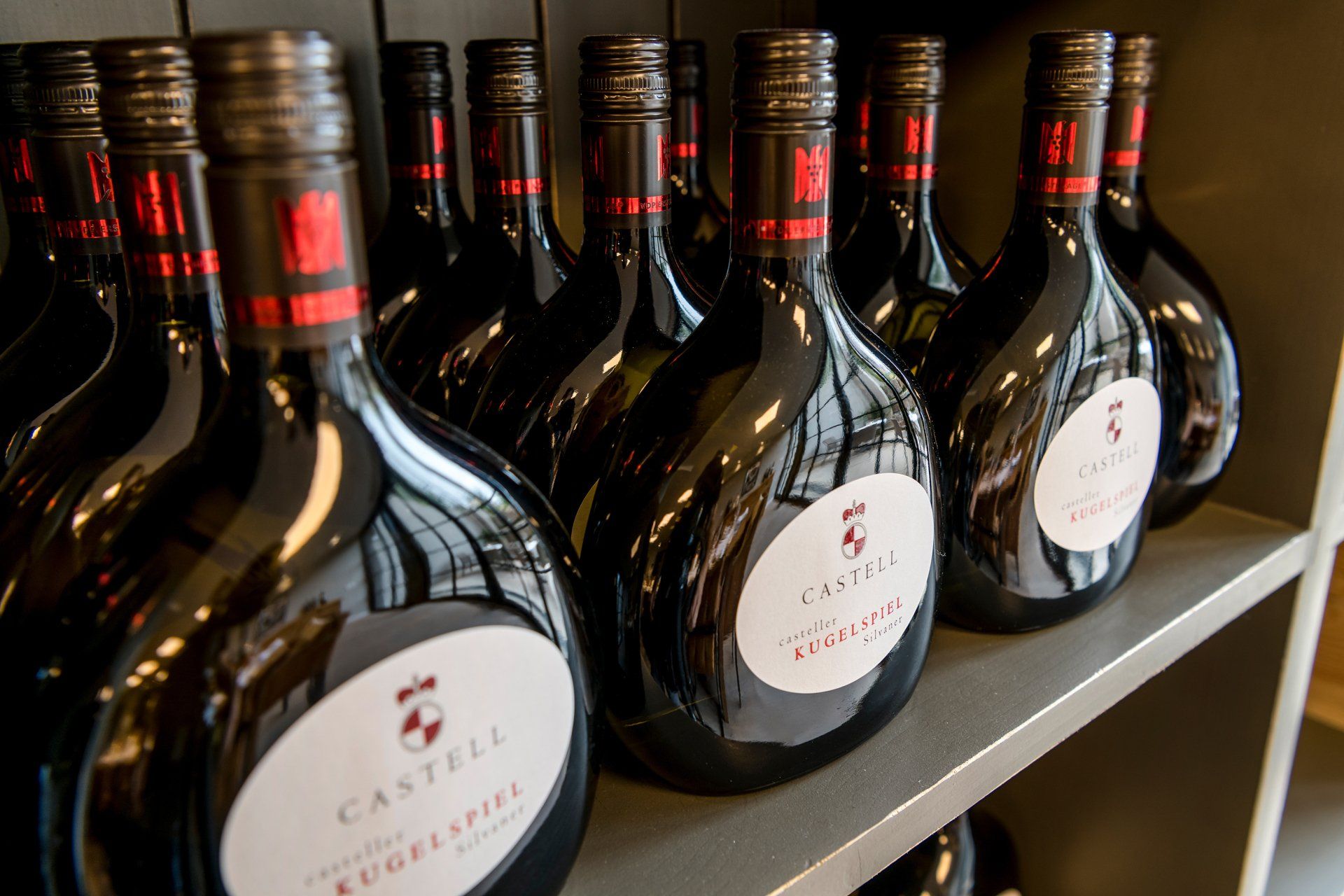 Eine Reihe Weinflaschen steht aufgereiht auf einem Regal.