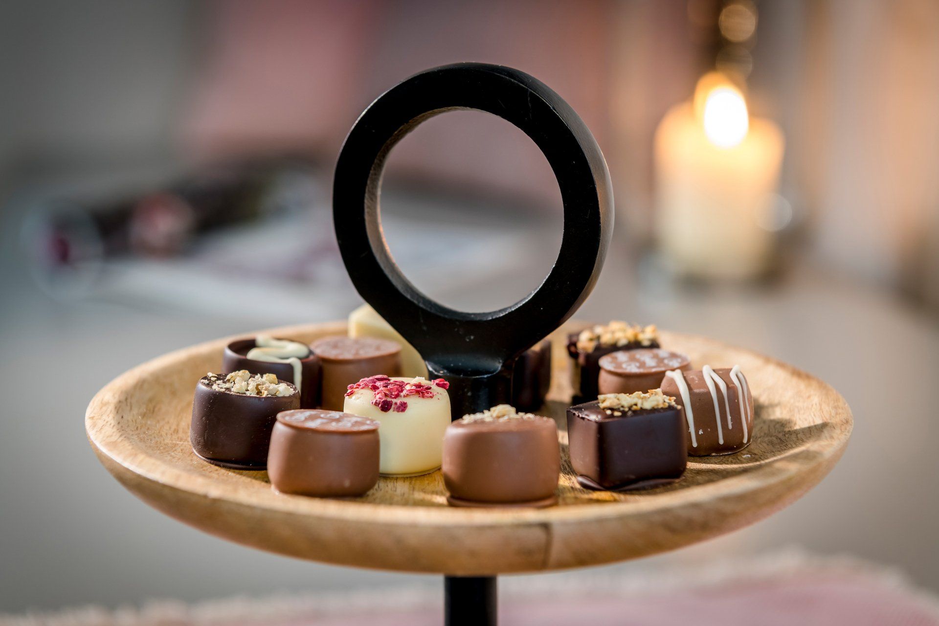 Ein Holztablett voller Pralinen und eine Kerze im Hintergrund.