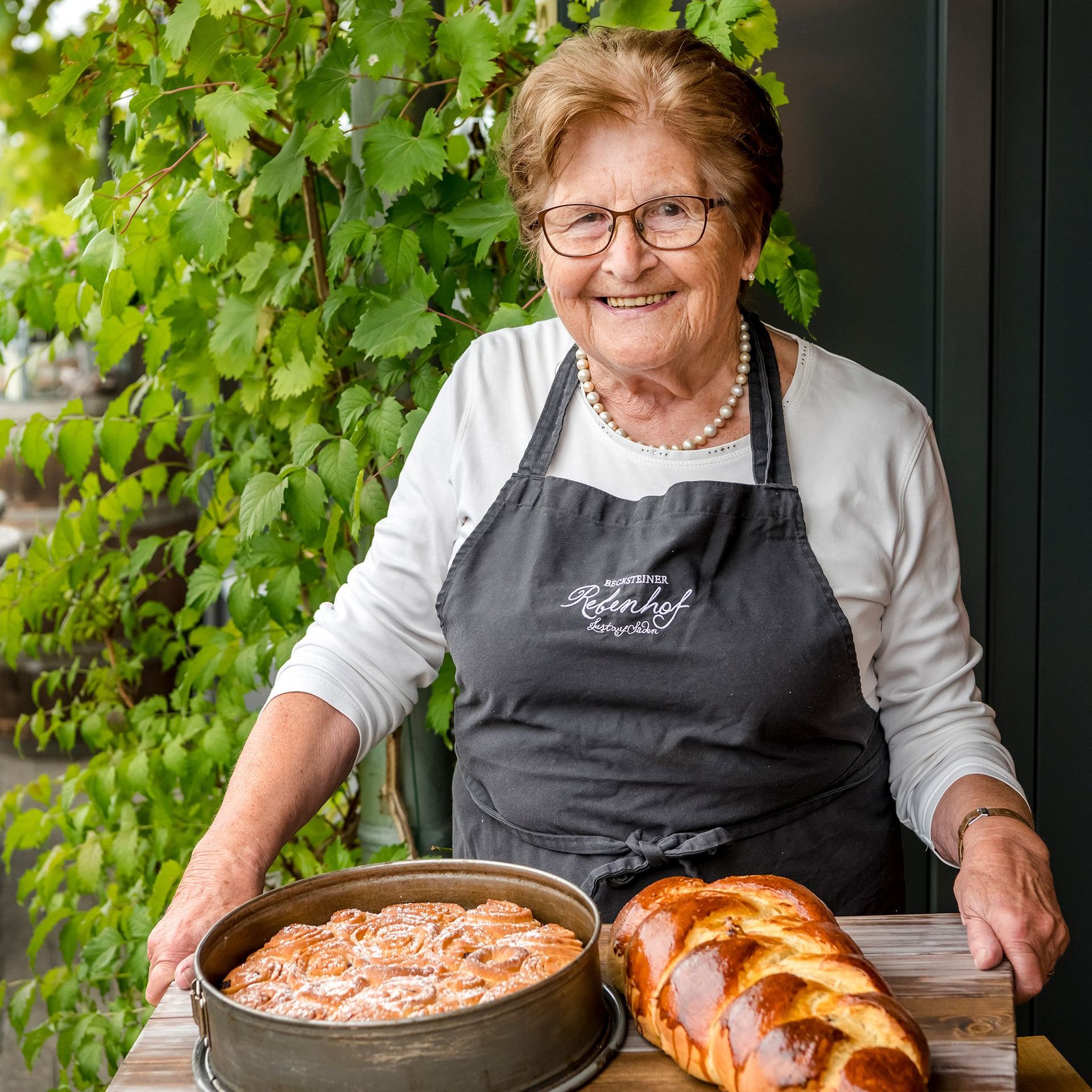 Eine Frau in einer Schürze hält einen Laib Brot und einen Kuchen.