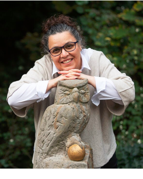 Eine Frau lehnt an einer Eulenstatue, die einen Apfel hält.