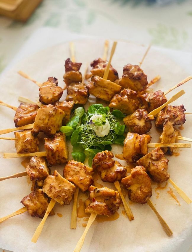 Un plato de brochetas de pollo con cebollas verdes encima