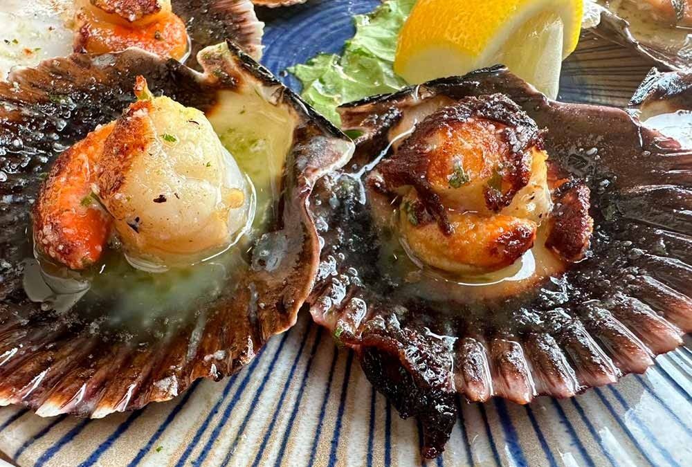 Un primer plano de un plato de comida con vieiras y limón sobre una mesa.