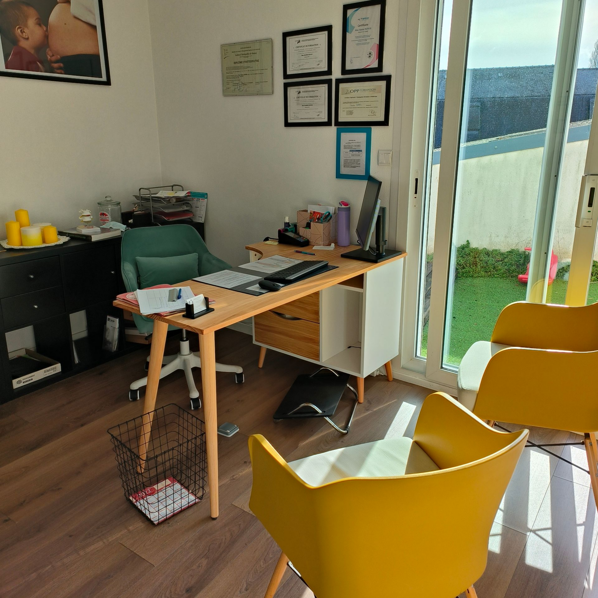 Bureau avec bureau, chaises, certificats au mur et vue sur un jardin.