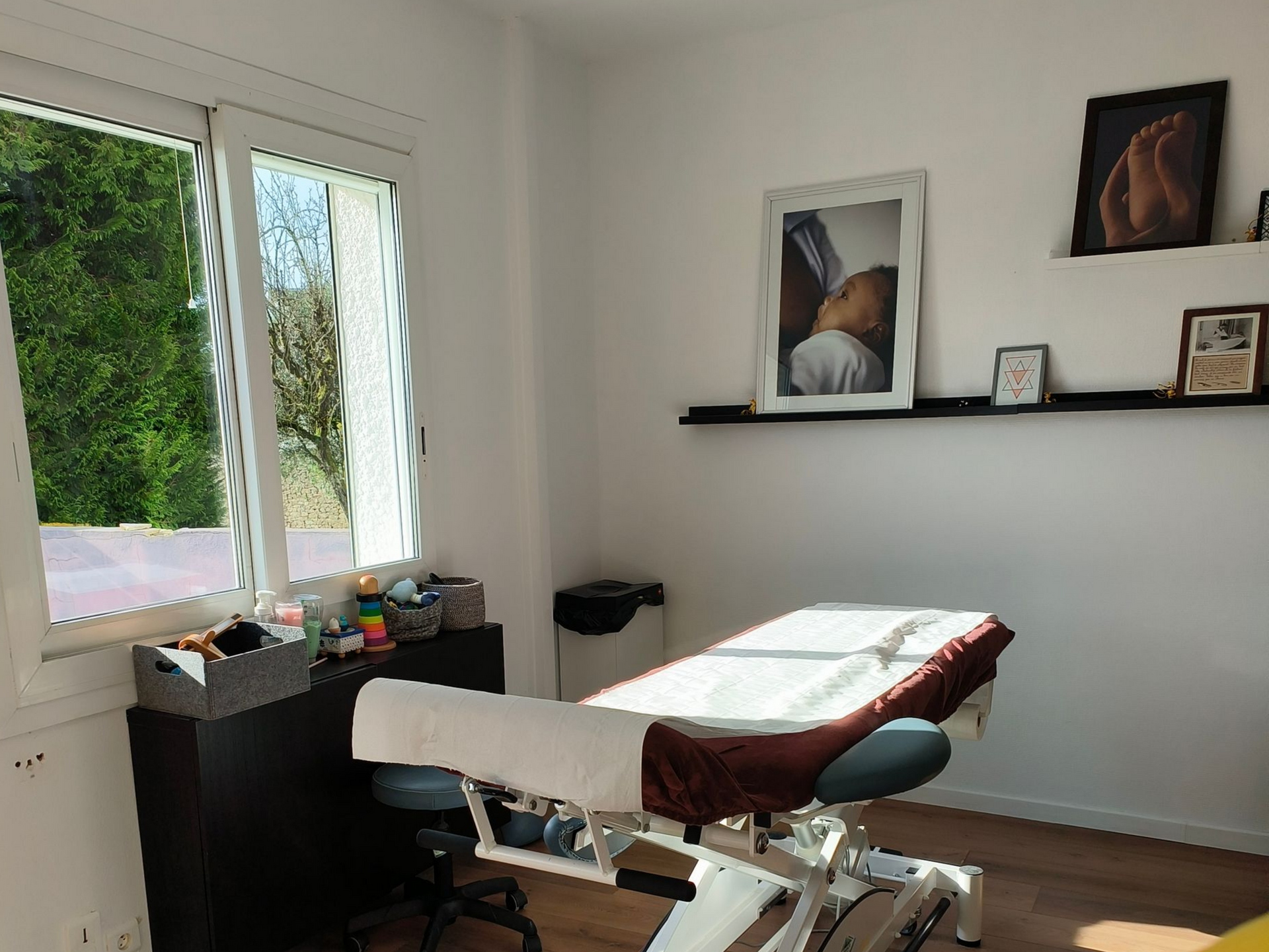 Une salle de massage avec un lit, une fenêtre ouverte et des étagères décoratives.