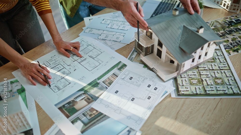 Gli architetti discutono i progetti di costruzione e un modellino di casa su un tavolo di legno, esaminando i disegni tecnici.