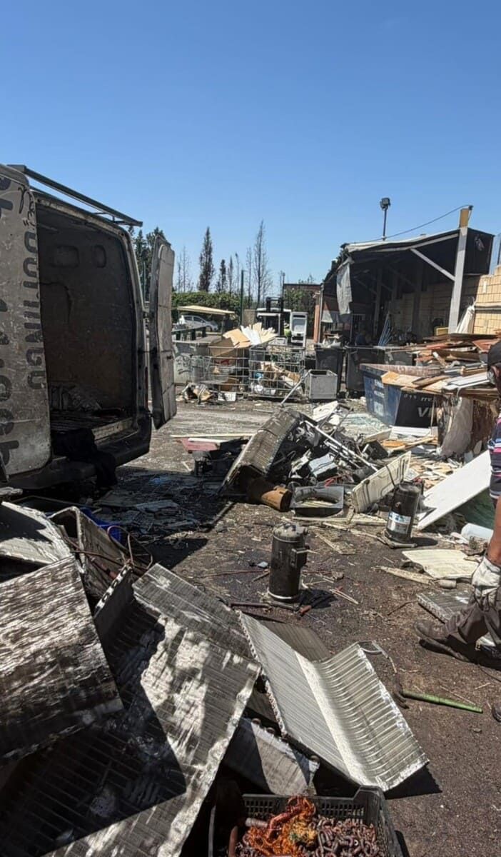 Escombros de edificios dañados por el fuego apilados al aire libre bajo un cielo azul despejado.