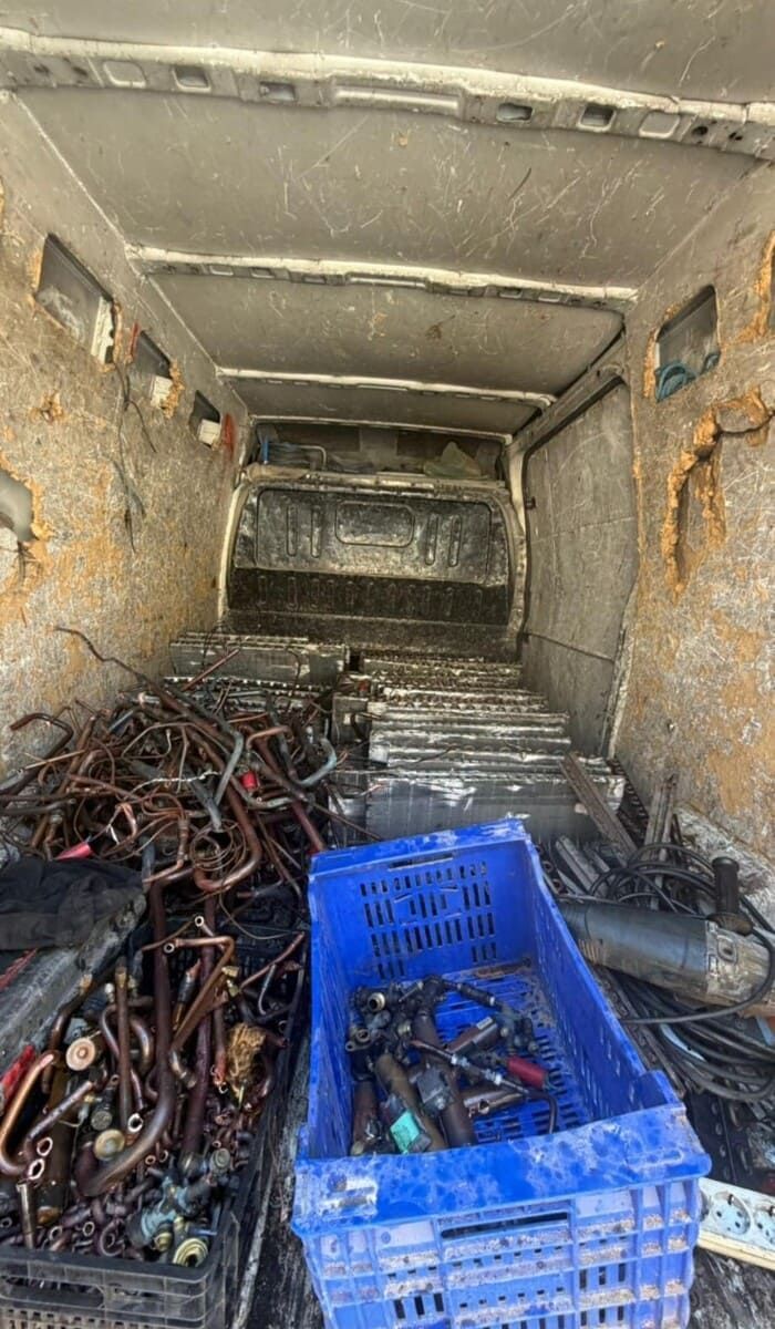 Dentro de un contenedor metálico, una caja azul y montones de cables enredados y chatarra llenan el suelo.
