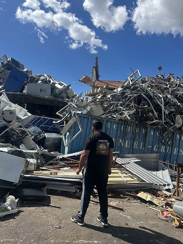 Un hombre de pie entre escombros y metal retorcido bajo un cielo azul brillante.