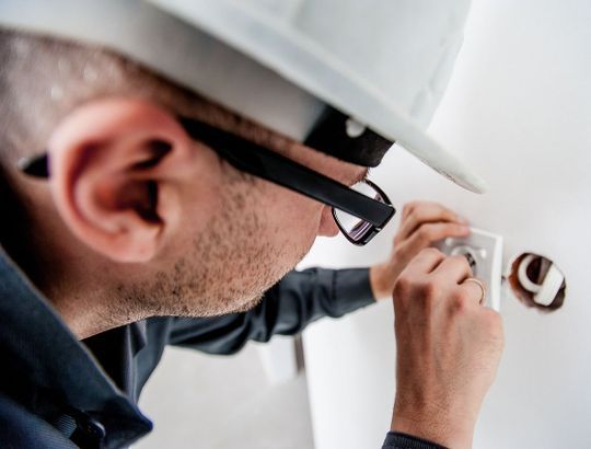 Un hombre que lleva casco y gafas está trabajando en una toma de corriente eléctrica.