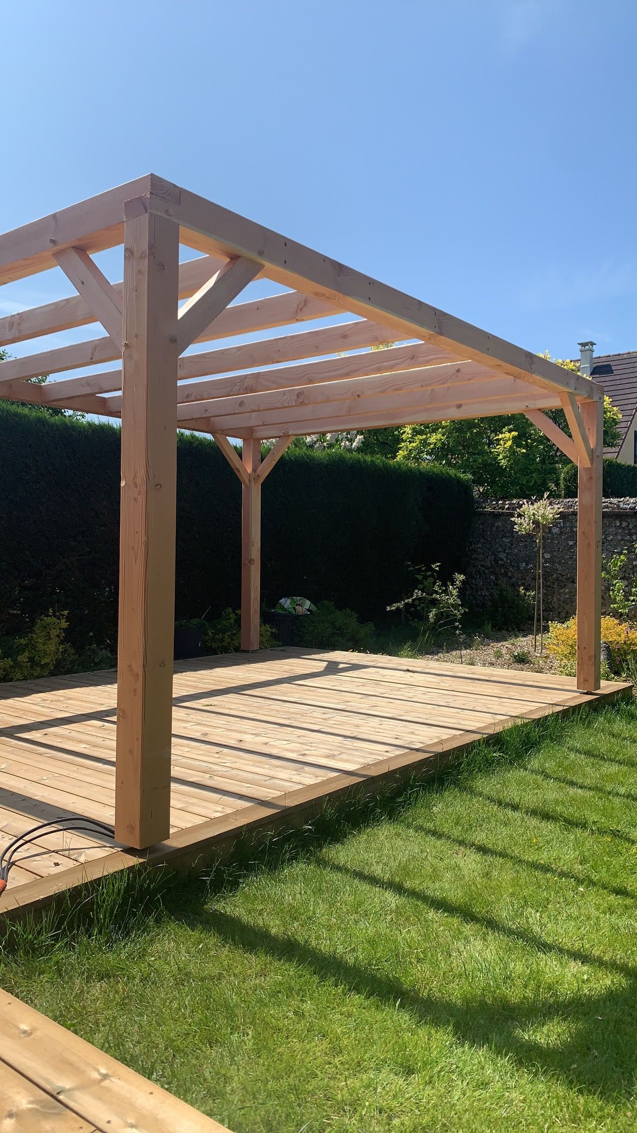 Pergola en bois dans un jardin ensoleillé, projetant des ombres sur la terrasse.