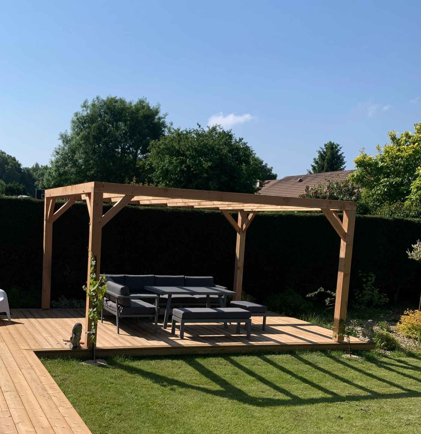 Pergola en bois au-dessus d'une terrasse avec sièges extérieurs dans un jardin ensoleillé.