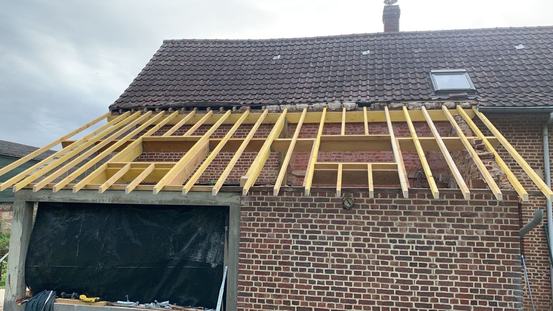 Un bâtiment en briques en construction, avec un toit partiellement enlevé et des supports en bois apparents.