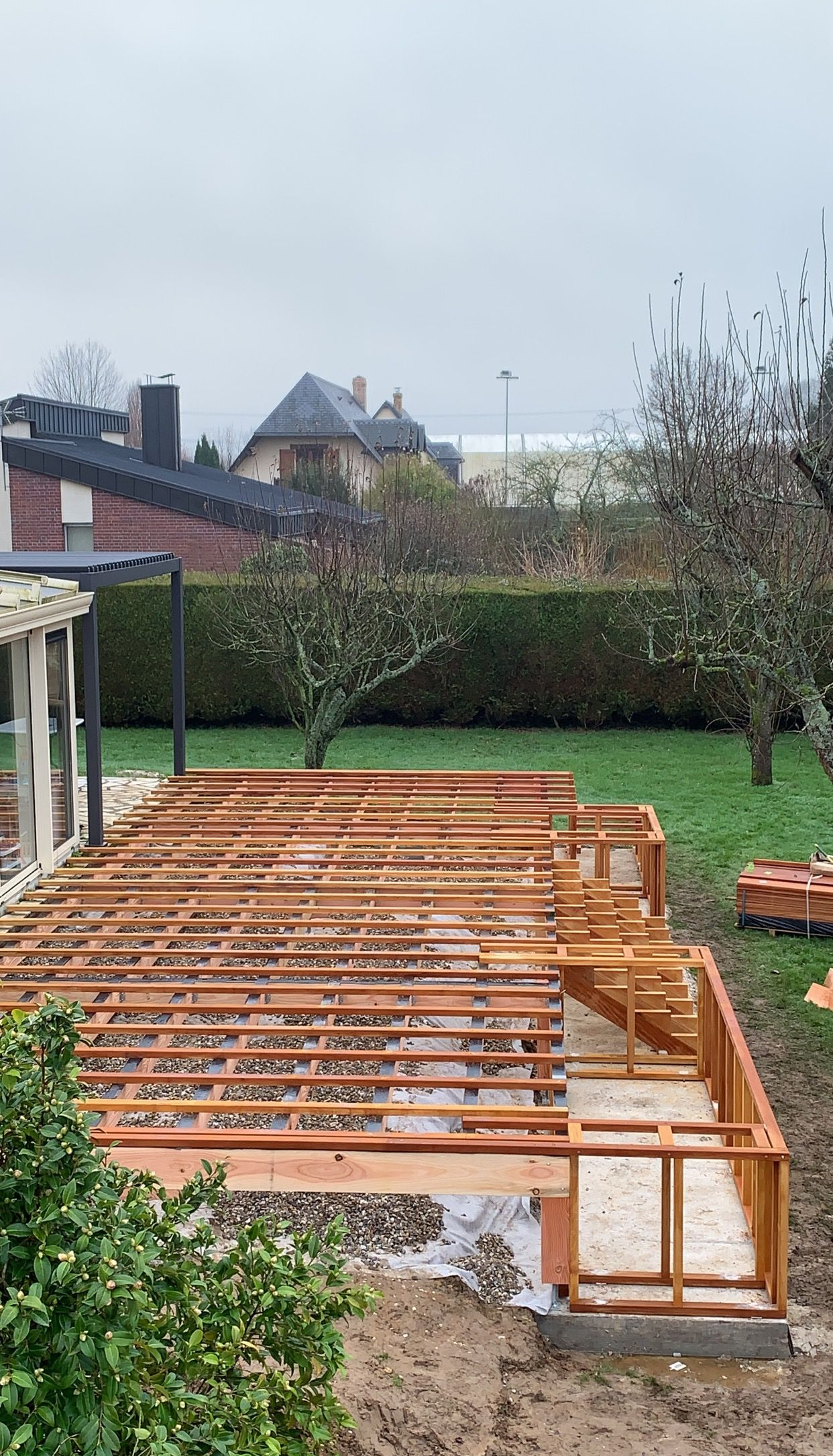 Construction d'une structure de terrasse en bois dans une cour arrière avec des arbres et des maisons en arrière-plan.