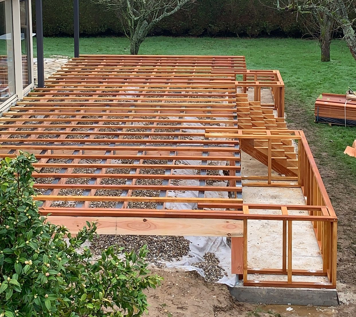 Terrasse en bois en construction avec solives apparentes, rambarde et escalier, située dans un jardin.