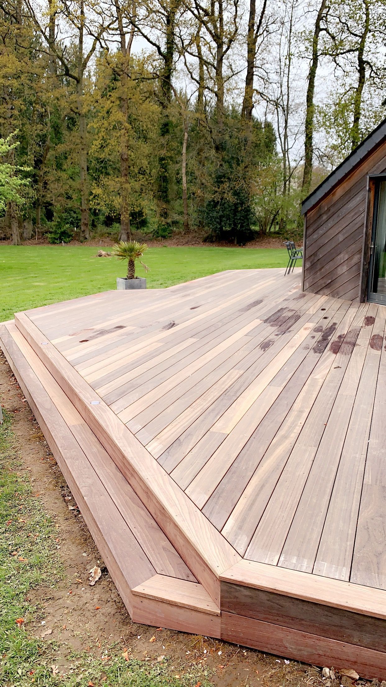 Terrasse en bois avec marches jouxtant un bâtiment, dans un cadre extérieur verdoyant.